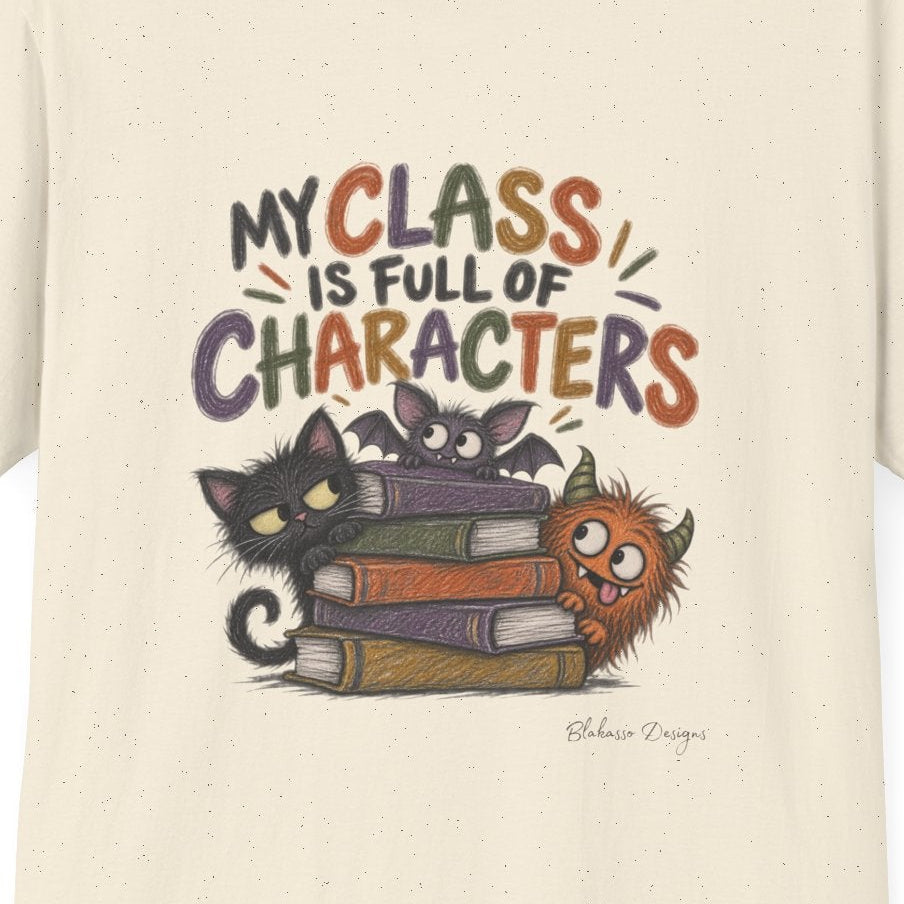 An off-white short-sleeve t-shirt with a colorful graphic on the front. The graphic features the text 'MY CLASS IS FULL OF CHARACTERS' above an illustration of a black cat, a purple cat, a stack of books, and a small orange monster.