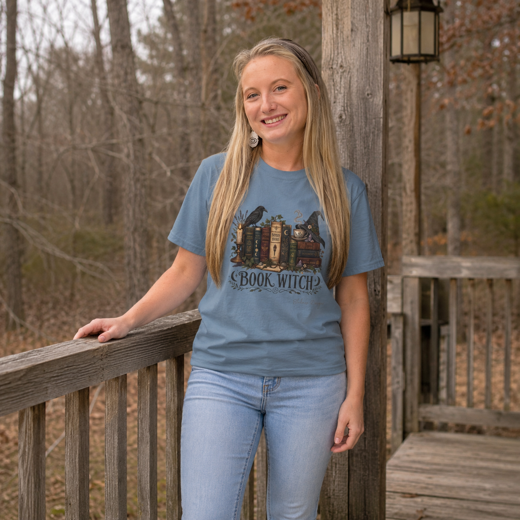 Blonde woman in rustic setting porch wearing a blue Book Witch design tshirt.