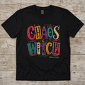 Black Chaos Witch T-shirt displayed on a weathered wood surface with colorful distressed lettering, celestial symbols, and eclectic witchy details.