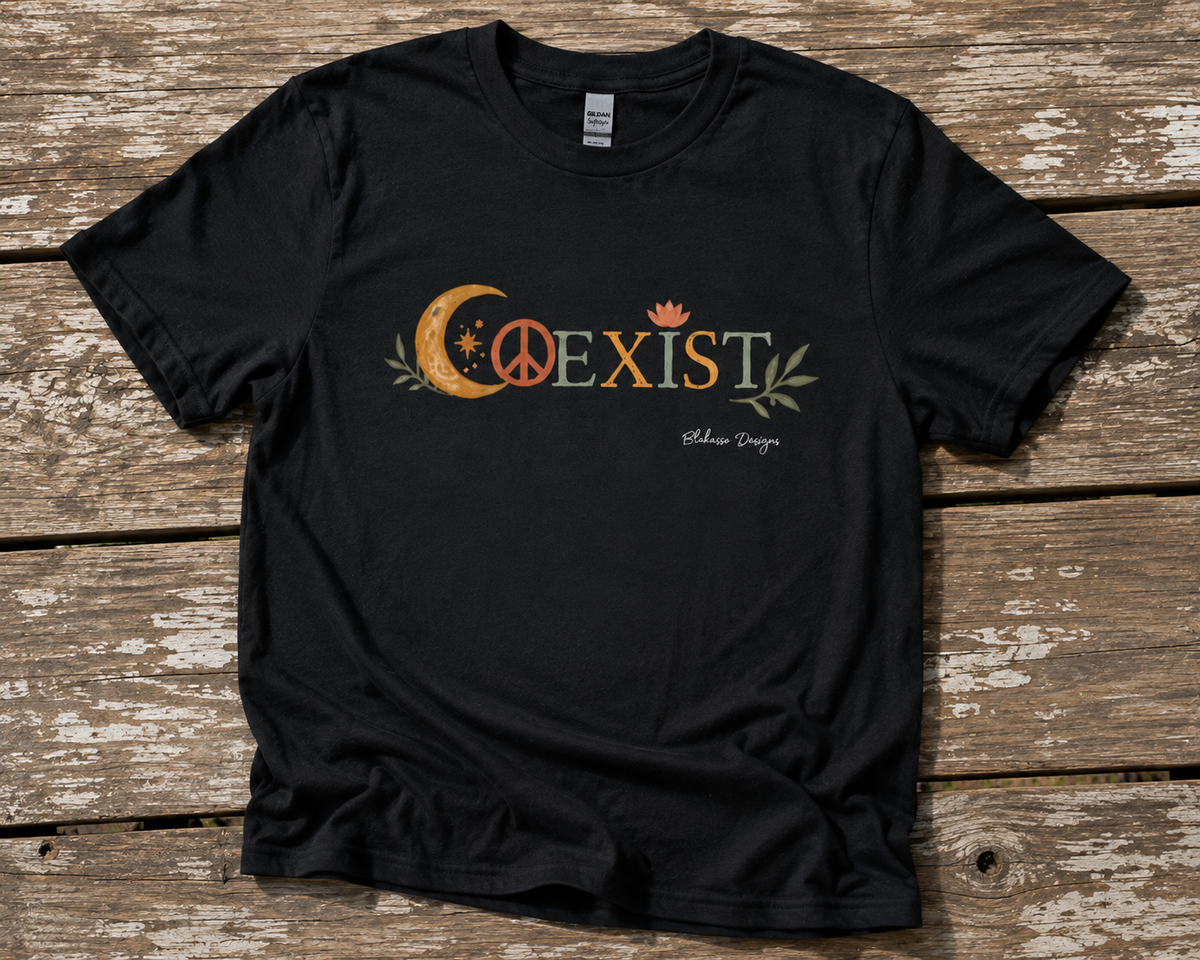 Black COEXIST unisex T-shirt displayed on a weathered wood surface with crescent moon, peace sign, lotus, and botanical artwork.