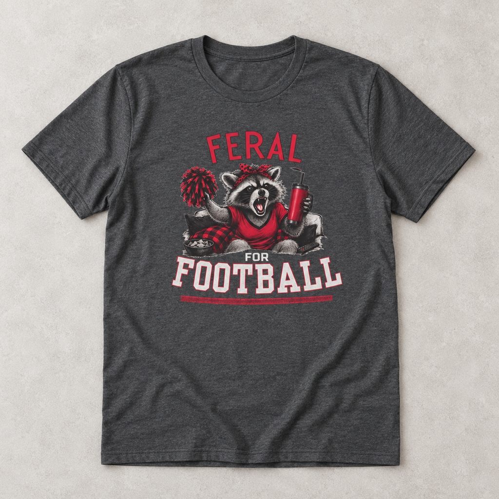 Dark heather Feral for Football Georgia T shirt flat lay featuring a cheering raccoon with a pom pom, drink tumbler, and bold red and white football graphic.