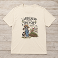 Natural unisex T-shirt featuring Sammye the raccoon gardener beside roses, fresh soil, and an Aqua Tofana Garden Club sign with the text “Gardening Doesn’t Have to Be Expensive. Reduce. Reuse. Recycle.”
