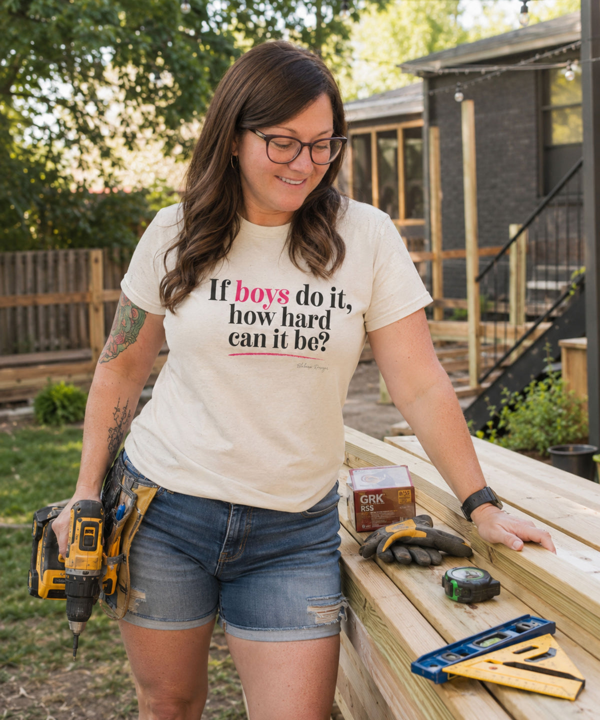 Woman wearing natural If Boys Do It How Hard Can It Be shirt while working with tools and lumber outdoors