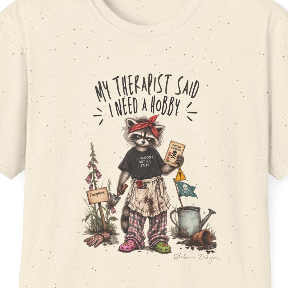 Close view of the raccoon poison garden artwork and “My Therapist Said I Need a Hobby” text on a T-shirt.