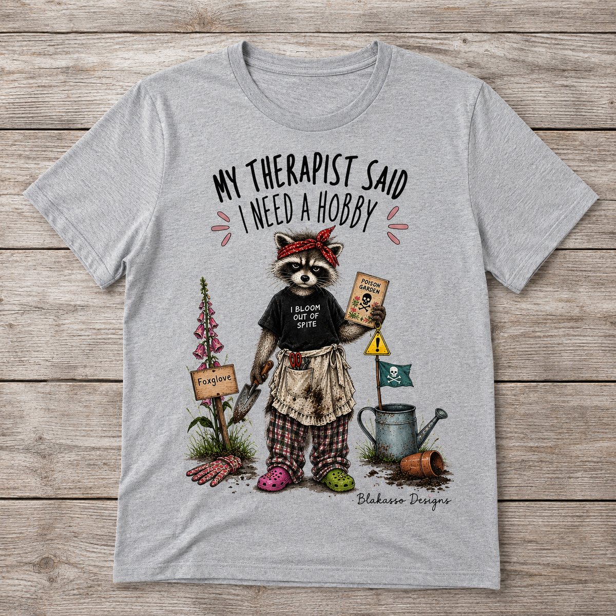 Sport Grey unisex T-shirt featuring a raccoon gardener with poison garden details and the text “My Therapist Said I Need a Hobby.”
