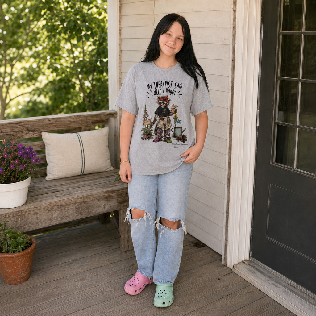 Young woman wearing a Sport Grey raccoon garden graphic T-shirt in a casual porch garden setting.