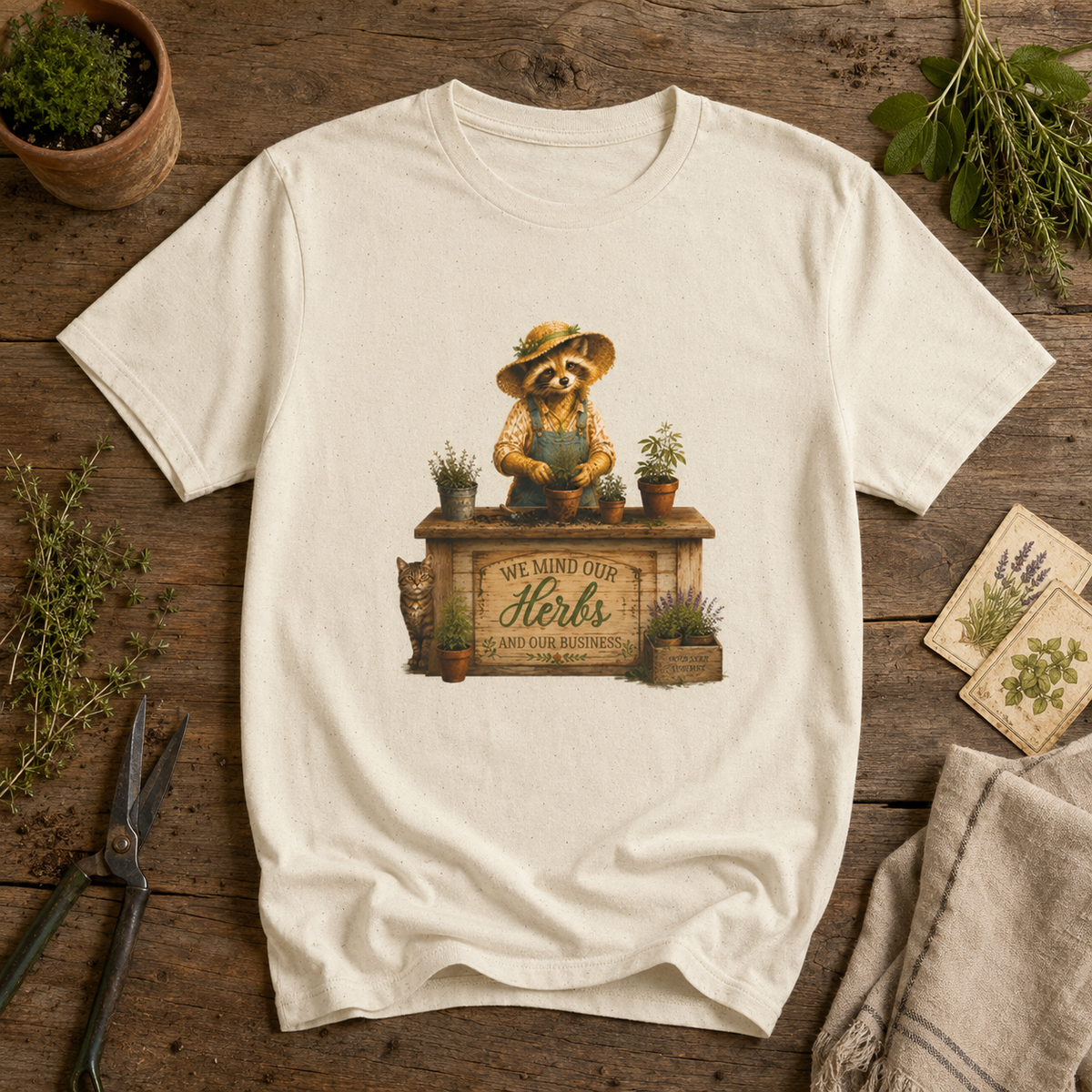 We Mind Our Herbs and Our Business Miss Sammye Raccoon Council graphic tee flat lay