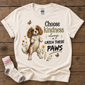 Natural T-shirt featuring the Choose Kindness Always or Catch These Paws Cavalier puppy design, styled with a stolen sock.