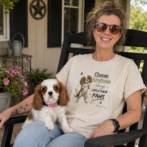 Woman wearing Choose Kindness Always or Catch These Paws T-shirt while sitting on a porch with a Cavalier King Charles Spaniel puppy.