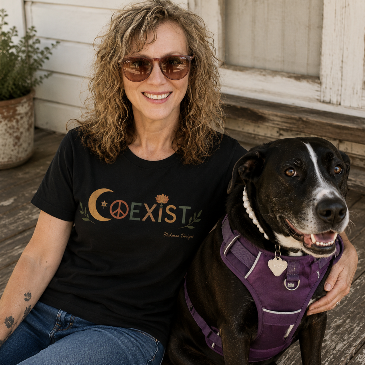 Woman wearing a black COEXIST T-shirt while sitting with her black and white dog Jazzy on a weathered porch.