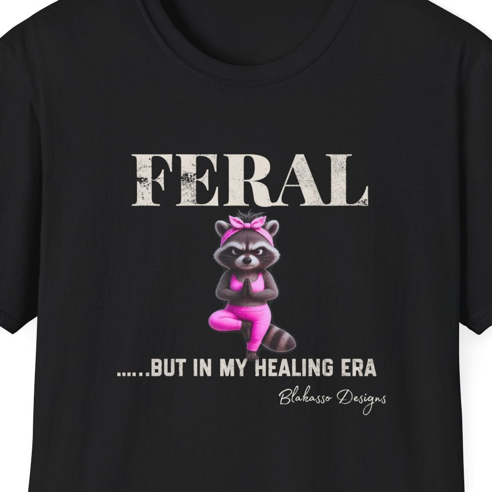 Close up of the “Feral...But In My Healing Era” design featuring a raccoon in pink yoga clothes balancing in tree pose.