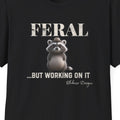 Close up of the "Feral...But Working On It" design featuring a whimsical raccoon wearing a tiny hat.