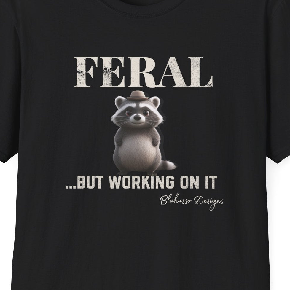 Close up of the "Feral...But Working On It" design featuring a whimsical raccoon wearing a tiny hat.