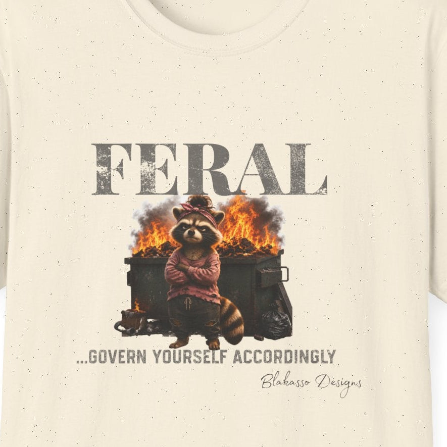 Close up of the “Feral...Govern Yourself Accordingly” design featuring an unimpressed raccoon standing in front of a burning dumpster.