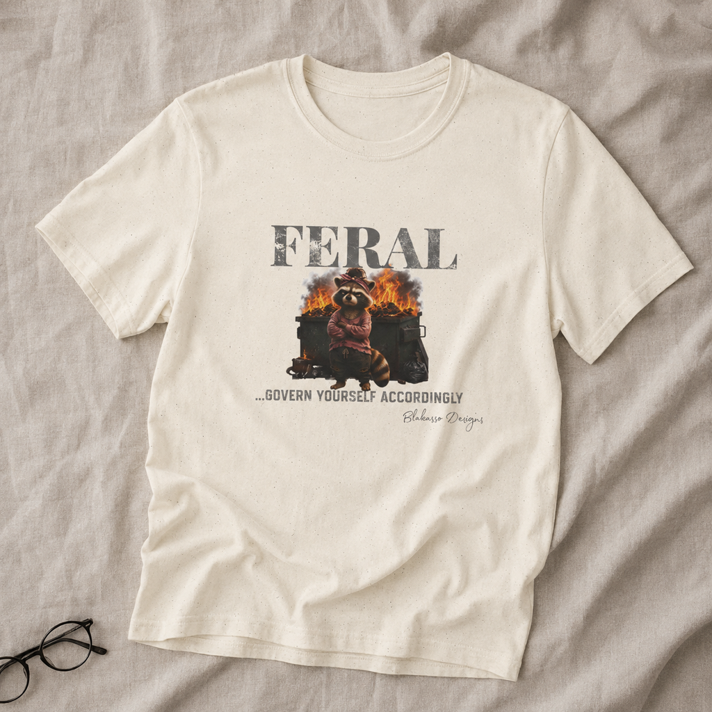 Natural unisex graphic tee featuring a raccoon standing in front of a burning dumpster with the words “Feral...Govern Yourself Accordingly.”