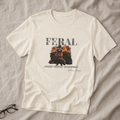 Natural unisex graphic tee featuring a raccoon standing in front of a burning dumpster with the words “Feral...Govern Yourself Accordingly.”