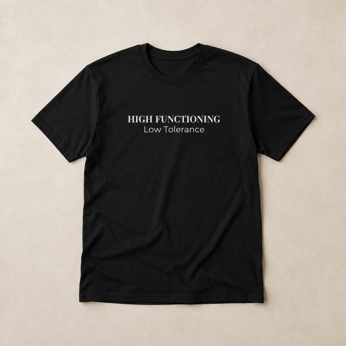 Black unisex tee laid flat on a warm neutral surface featuring the High Functioning Low Tolerance text design across the chest.