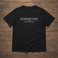 Black unisex tee laid flat on a warm wood surface featuring the Overeducated Under Rested design across the chest.