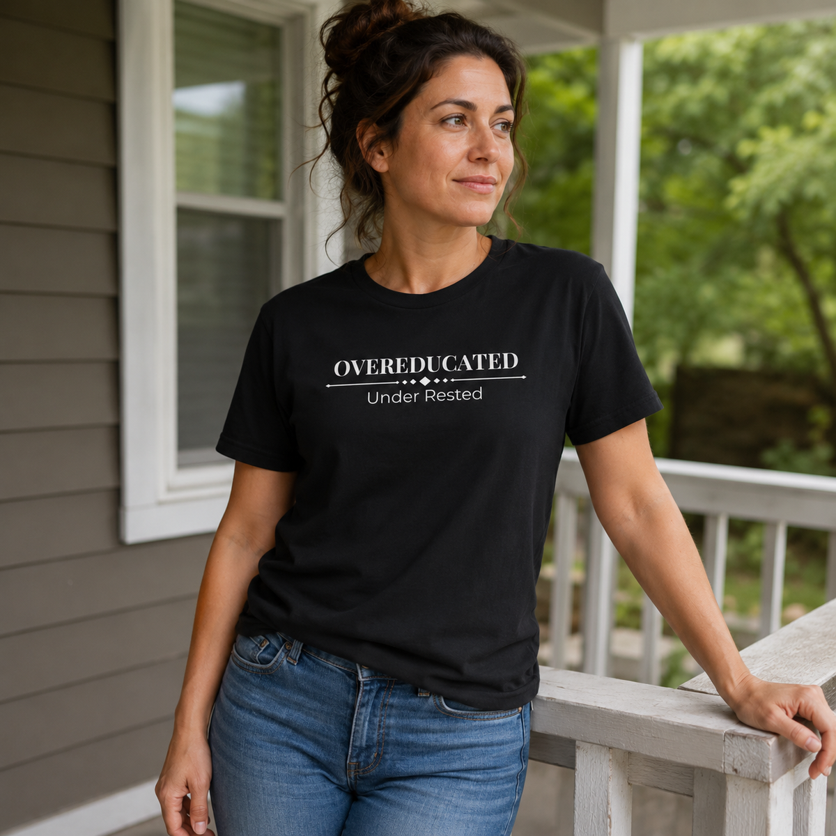 Woman wearing a black Overeducated Under Rested unisex tee while standing casually on a porch.