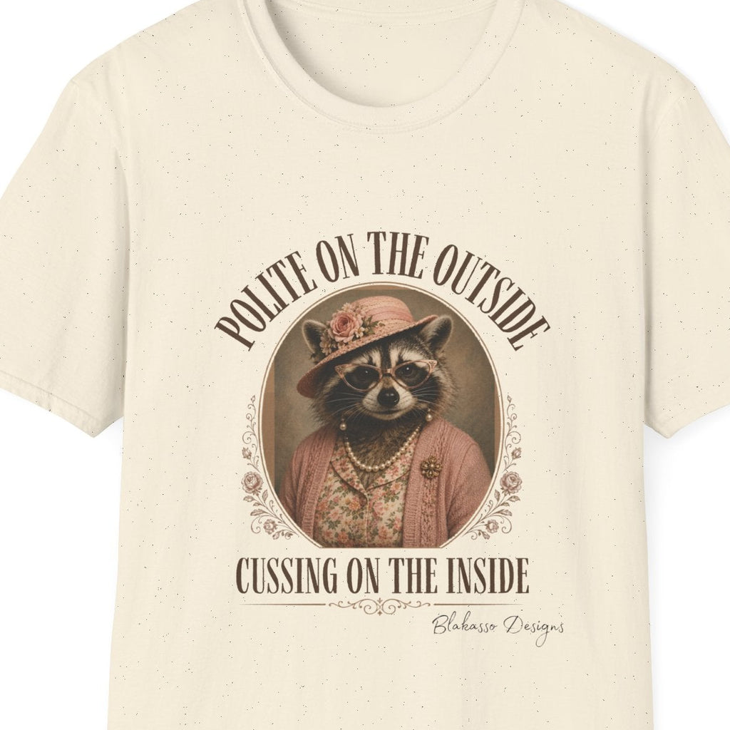 Close up of the Miss Cordelia raccoon design on a natural tee featuring her pink hat, pearls, cat eye glasses, and “Polite on the Outside, Cussing on the Inside” text.