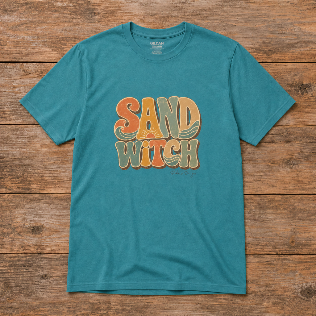 Flat lay of a Heather Galapagos Blue Sand Witch T-shirt featuring retro lettering in orange, mustard, cream, and seafoam with sun and wave details.