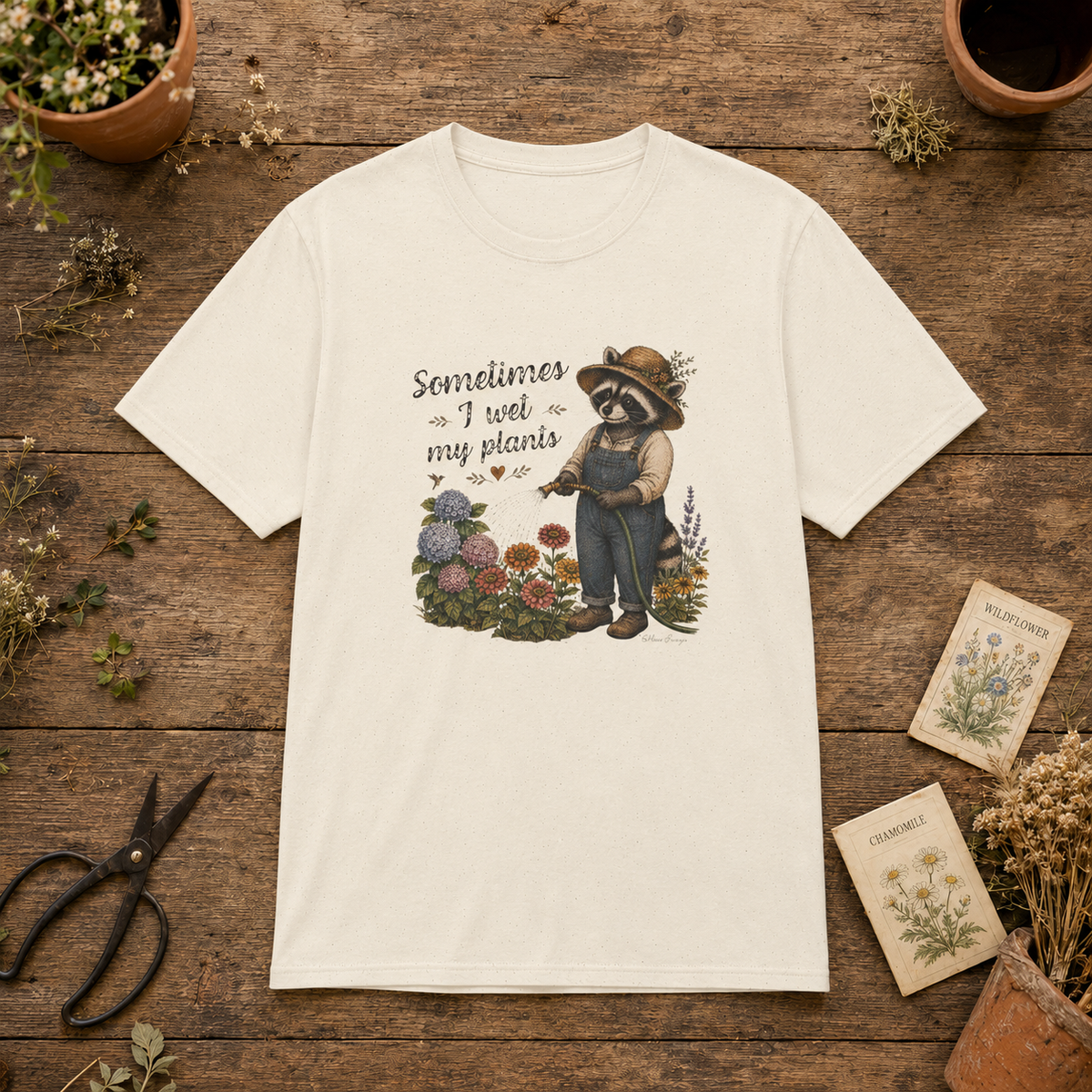 Natural Sometimes I Wet My Plants tee featuring Miss Sammye the gardening raccoon watering hydrangeas, zinnias, and colorful flowers.