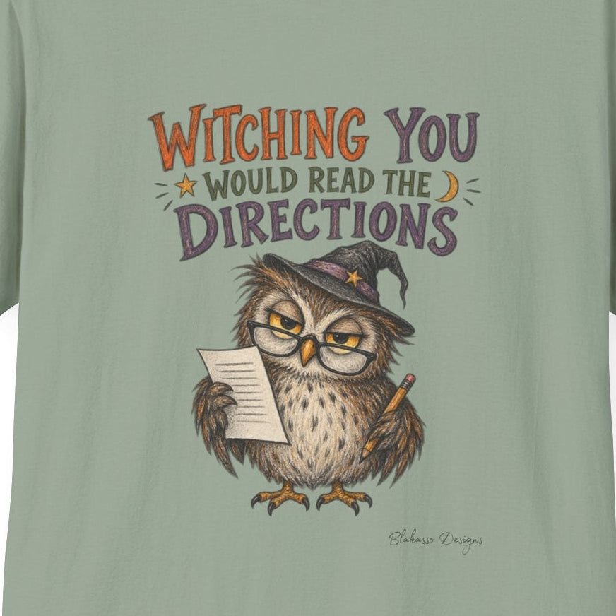 A sage green crewneck t-shirt featuring a graphic of an owl wearing a witch hat and holding a map, with the text 'WITCHING YOU WOULD READ THE DIRECTIONS' in orange and purple lettering.